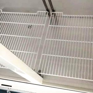 Two white metal-wire shelves, situated vertically side-by-side, with vertical support tracks against a wall in an empty storage area.