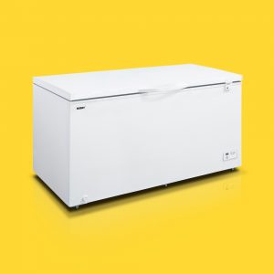A large white chest freezer sits on a glossy surface against a bright yellow background.