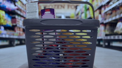 Grocery shopping basket in a supermarket aisle with shelves and a commercial display fridge in the background