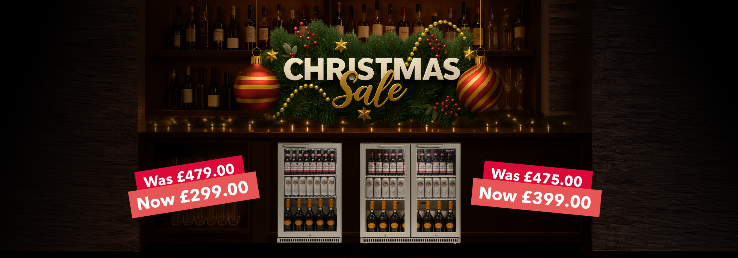 A festive Christmas sale banner showing two silver Husky back bar fridges fully stocked with drinks. Above them is a decorated garland with baubles, lights, and the text “Christmas Sale” in gold and white. Red price tags display discounted offers: “Was £479.00 Now £299.00” on the left and “Was £475.00 Now £399.00” on the right. Bottles of wine are arranged on shelves in the background.