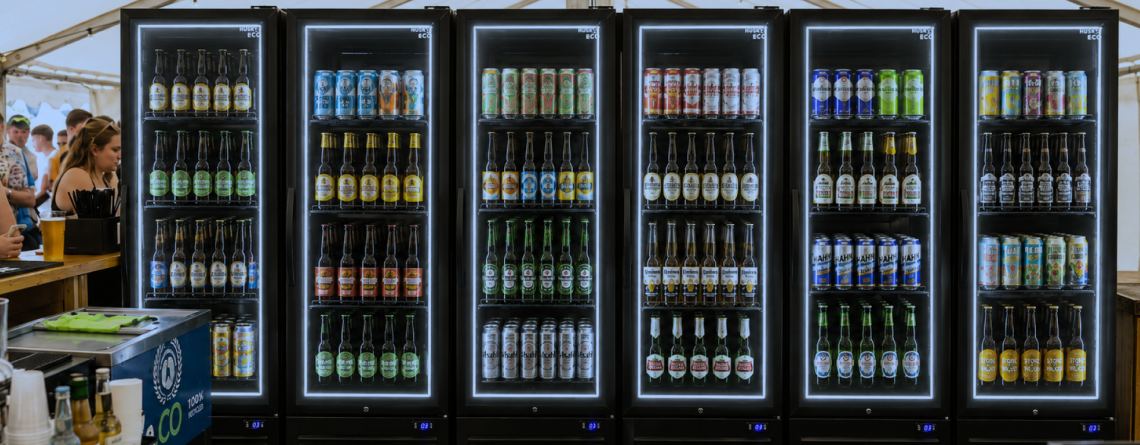 Husky drinks fridges stocked with beers and canned beverages at a busy festival bar, showcasing illuminated commercial drinks fridges for high-volume event service.