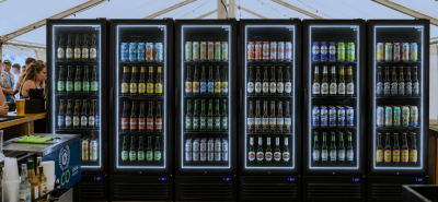 Husky drinks fridges stocked with beers and canned beverages at a busy festival bar, showcasing illuminated commercial drinks fridges for high-volume event service.